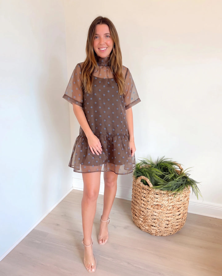 A woman modeling a brown sheer mesh mini dress with blue polka dots.
